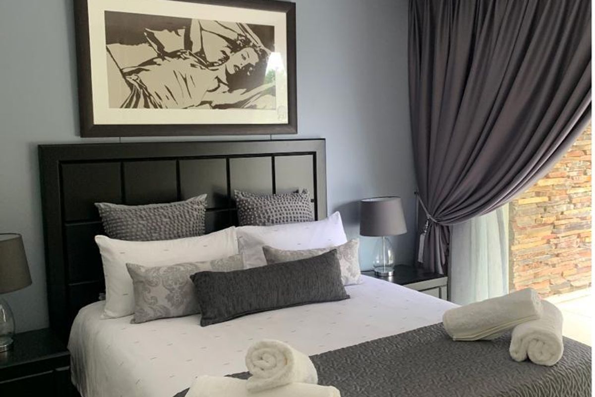 A well-maintained bedroom featuring neutral wall tones, recessed downlighting, and direct access to an outdoor area with stone feature walling.