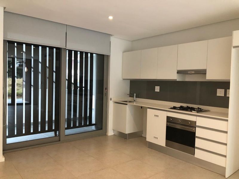 Modern kitchen featuring sleek white cabinetry, stone countertops, integrated gas hob, oven, and extractor fan, with large sliding doors providing natural light.