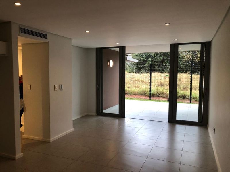 A bright, open-plan living area featuring large format floor tiles, recessed lighting, and sliding glass doors leading to an outdoor patio space.