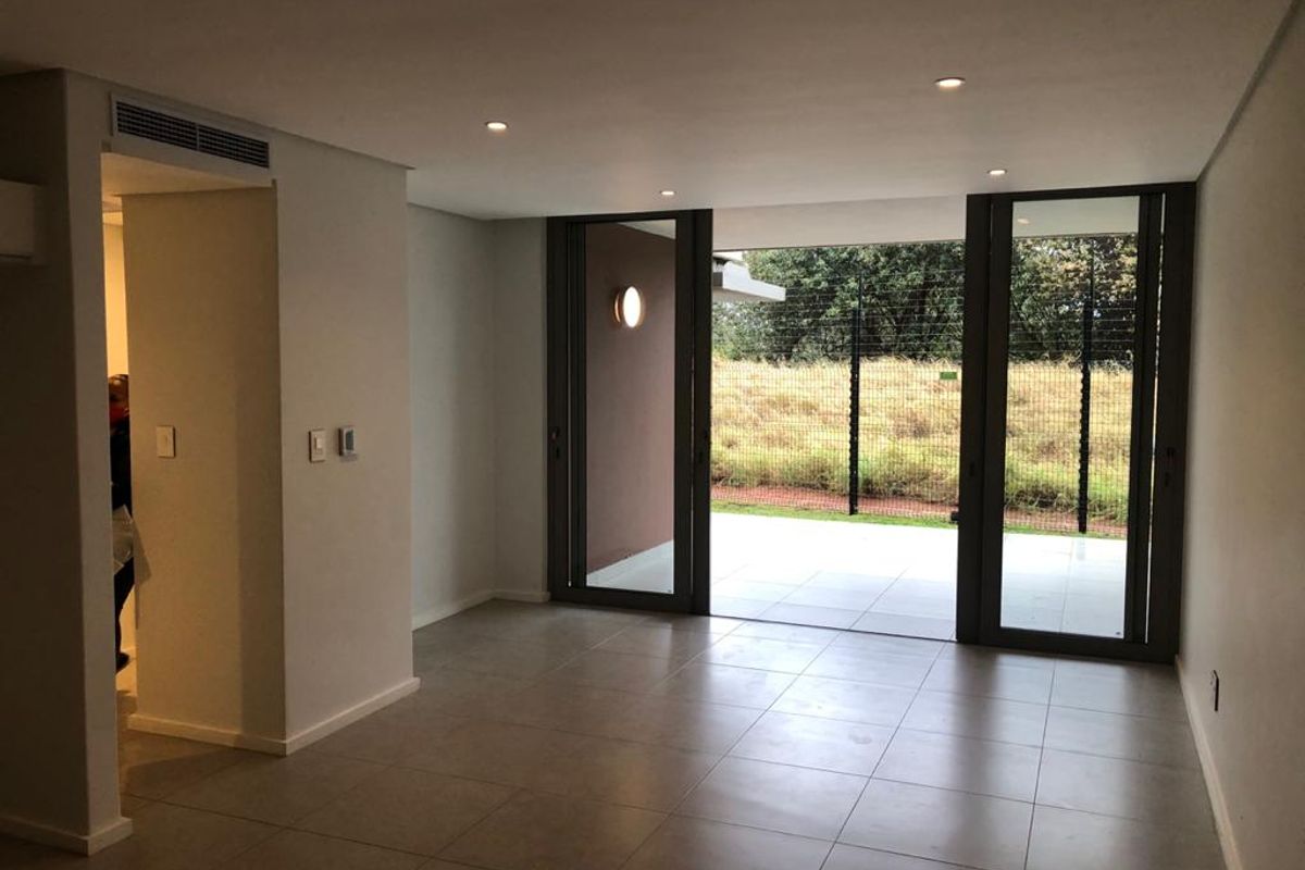 A bright, open-plan living area featuring large format floor tiles, recessed lighting, and sliding glass doors leading to an outdoor patio space.