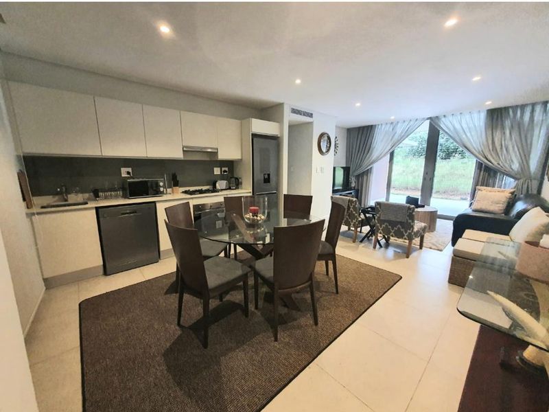 Modern open-plan living area featuring a sleek kitchen with integrated appliances, tiled flooring, and large sliding doors leading to an outdoor space.