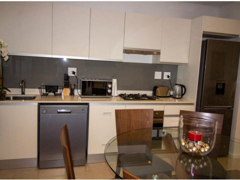 Modern kitchen featuring sleek white cabinetry, stone countertops, a glass splashback, and integrated stainless steel appliances including a gas hob and oven.
