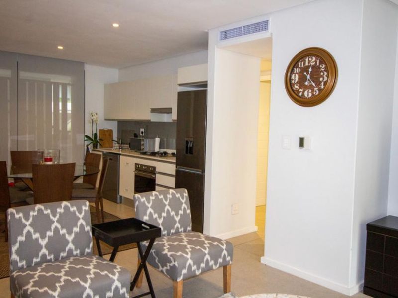 Modern open-plan apartment living area featuring a sleek kitchen with built-in appliances, tiled flooring, and ducted air conditioning.