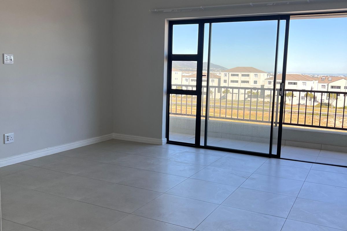 A bright, empty living room featuring large format floor tiles, recessed lighting, and a large sliding glass door leading to a balcony with scenic views.
