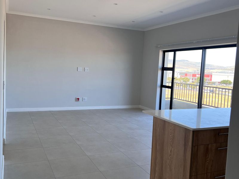 Spacious open-plan living area featuring modern tiled floors, recessed lighting, and a kitchen island with stone countertops, leading to a balcony with scenic views.