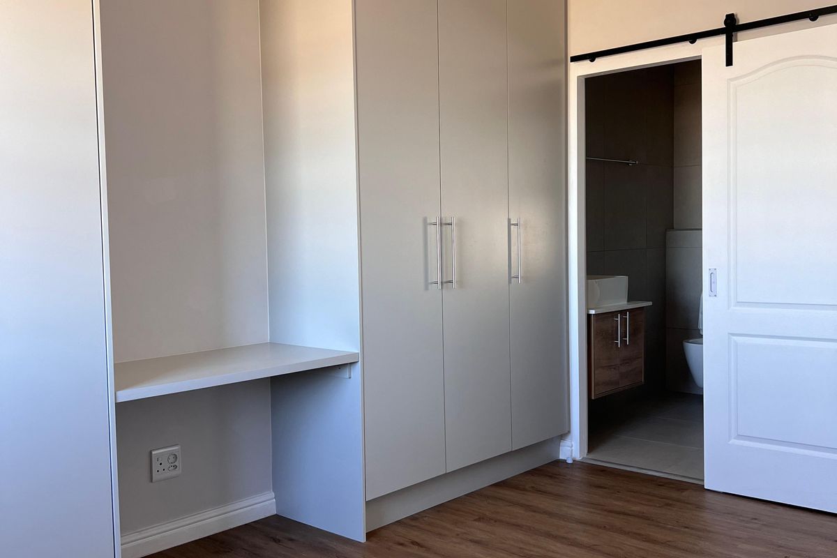 A bright, modern bedroom featuring built-in cupboards, a integrated desk, and a sliding barn door leading to an en-suite bathroom.