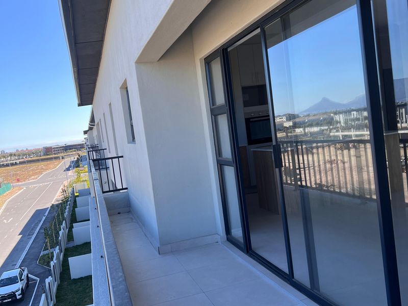 A modern apartment balcony featuring tiled flooring, a sleek metal balustrade, and large sliding glass doors providing access to the interior living space.