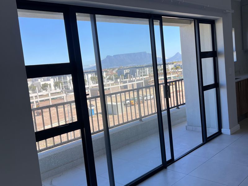Open plan living area featuring large sliding glass doors leading to a balcony with scenic mountain views and modern tiled flooring.