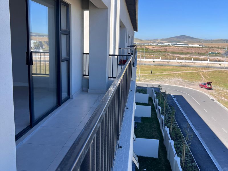 A modern apartment balcony featuring tiled flooring, a metal balustrade, and sliding glass doors, offering an elevated view of the surrounding landscape.