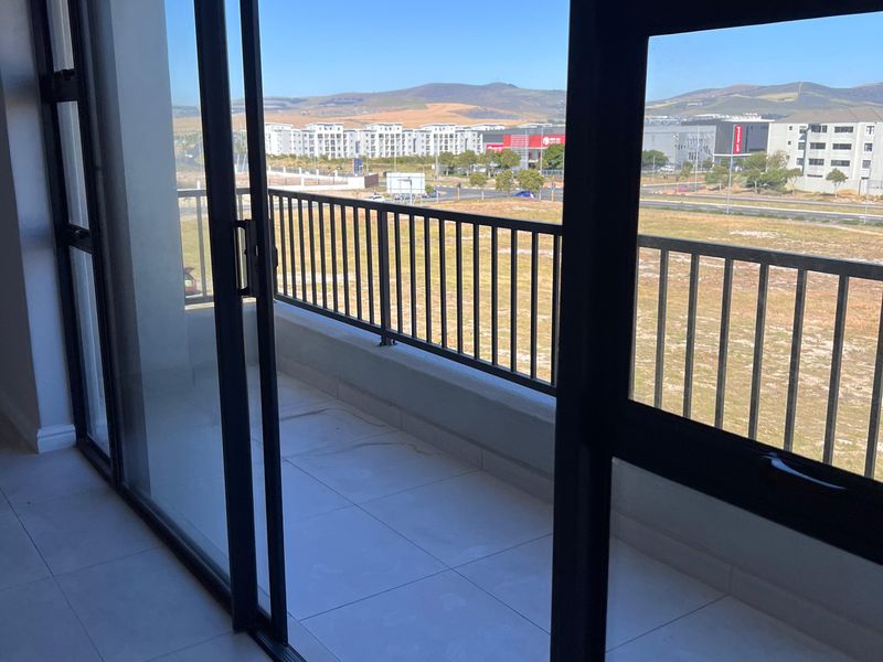 A clean, modern balcony featuring tiled flooring, black-framed sliding glass doors, and a metal balustrade with expansive views of the surrounding area.