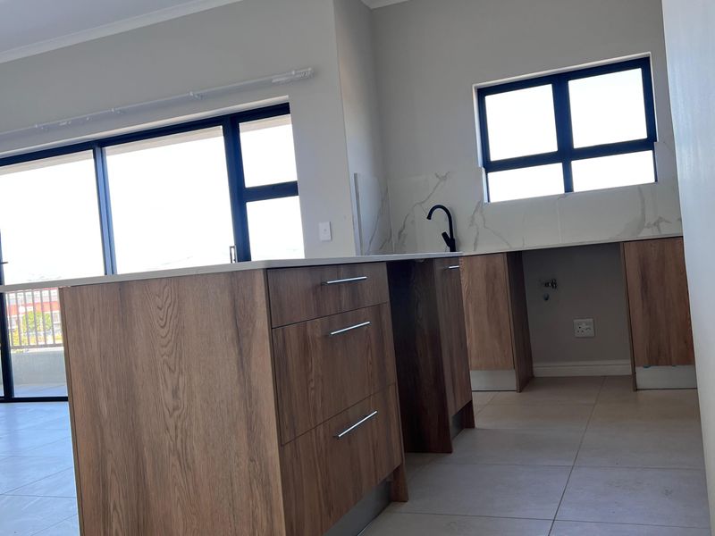 Modern kitchen featuring a central island with wood-finish cabinetry, stone countertops, and a sleek black tap, opening onto a balcony area.