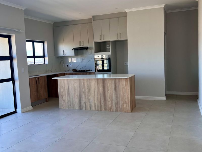 Modern open-plan kitchen featuring a central island, built-in oven, extractor fan, and neutral cabinetry, set within a spacious, tiled living area.