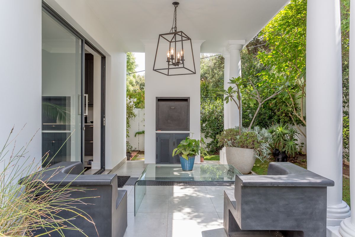 A covered patio featuring a built-in braai, tiled flooring, and elegant columns, providing a seamless transition to the garden area.