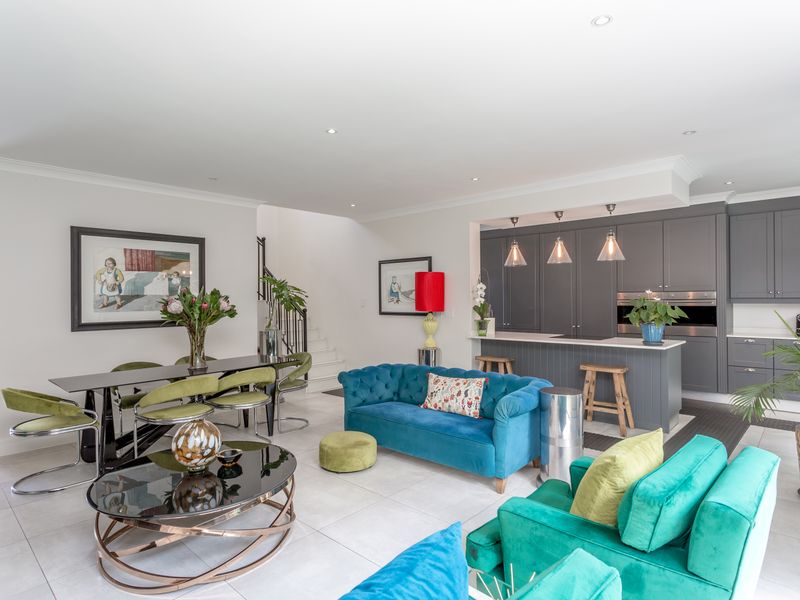 Spacious open-plan living and dining area featuring a modern grey kitchen with an island, recessed lighting, and neutral tiled flooring throughout.