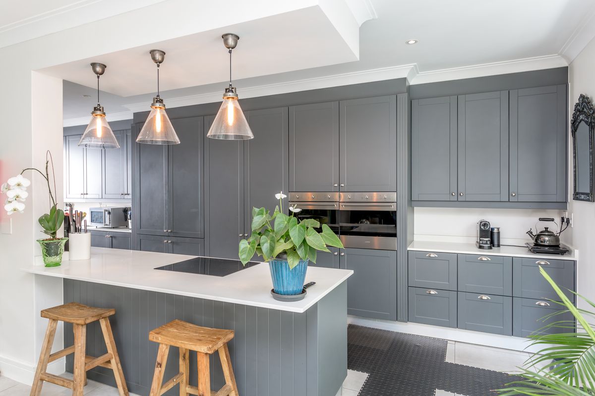 Modern kitchen featuring dark grey cabinetry, a central island with stone countertops, built-in double ovens, and stylish pendant lighting.