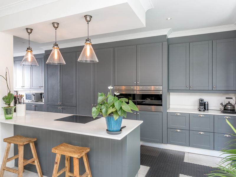 Modern kitchen featuring dark grey cabinetry, a central island with stone countertops, built-in double ovens, and stylish pendant lighting.