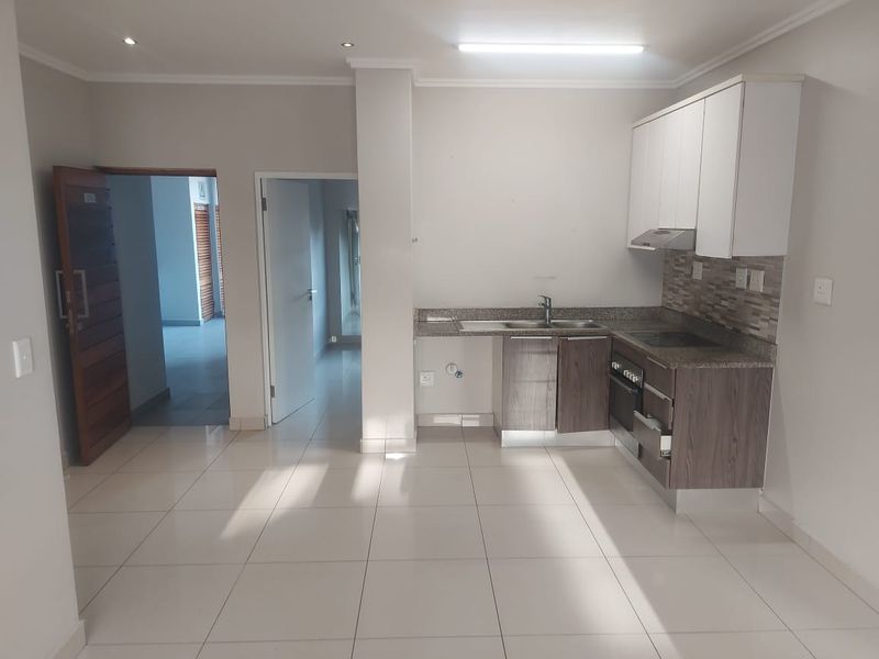 Open-plan kitchen area featuring modern cabinetry, stone countertops, integrated appliances, and neutral tiled flooring, providing a clean and functional space.
