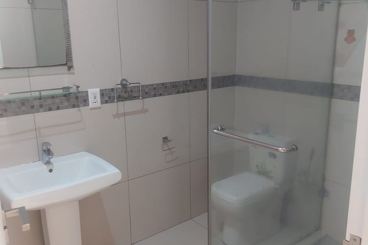A clean, modern bathroom featuring a pedestal washbasin, a glass-enclosed shower, and a toilet with neutral wall and floor tiling.