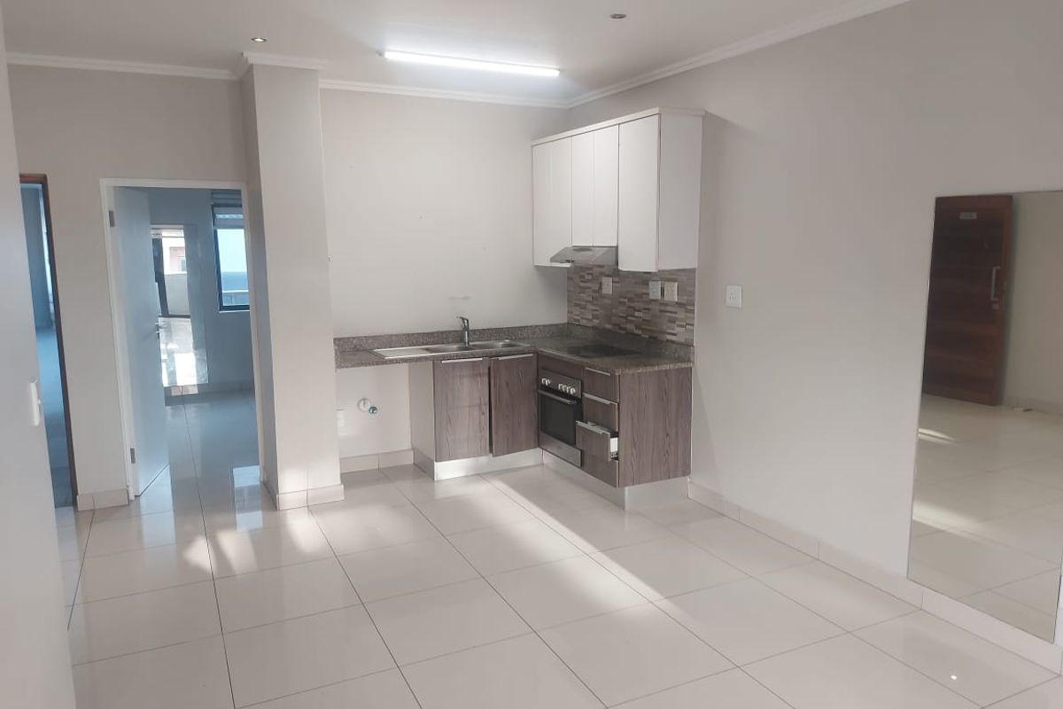 A clean, modern kitchen featuring built-in cabinetry, stone countertops, and integrated appliances, set within an open-plan living space with neutral tiled flooring.