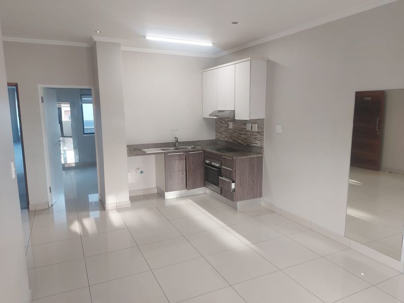 A clean, modern kitchen featuring built-in cabinetry, stone countertops, and integrated appliances, set within an open-plan living space with neutral tiled flooring.