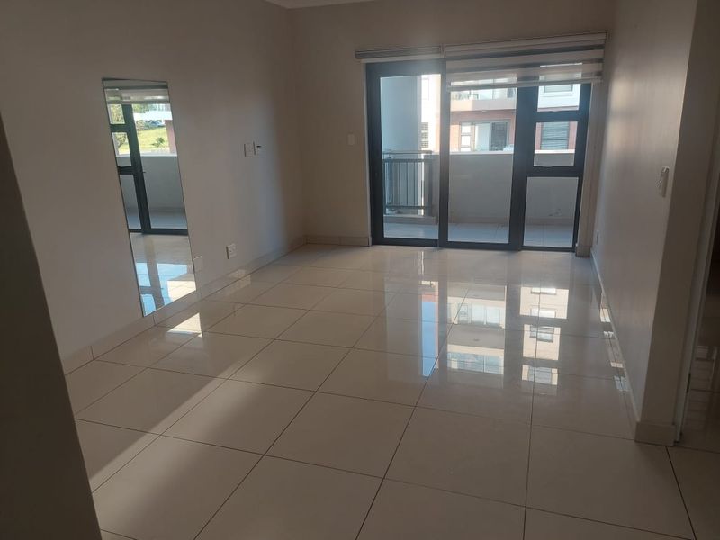 A bright, empty living room featuring polished tiled flooring and a large sliding glass door providing access to an outdoor balcony.