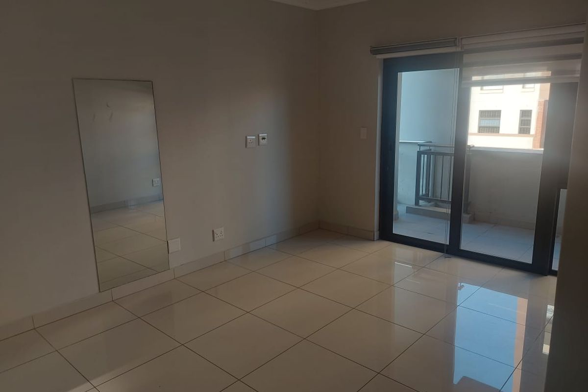 A bright, empty living area featuring neutral tiled flooring, recessed lighting, and a sliding glass door providing access to a private balcony.