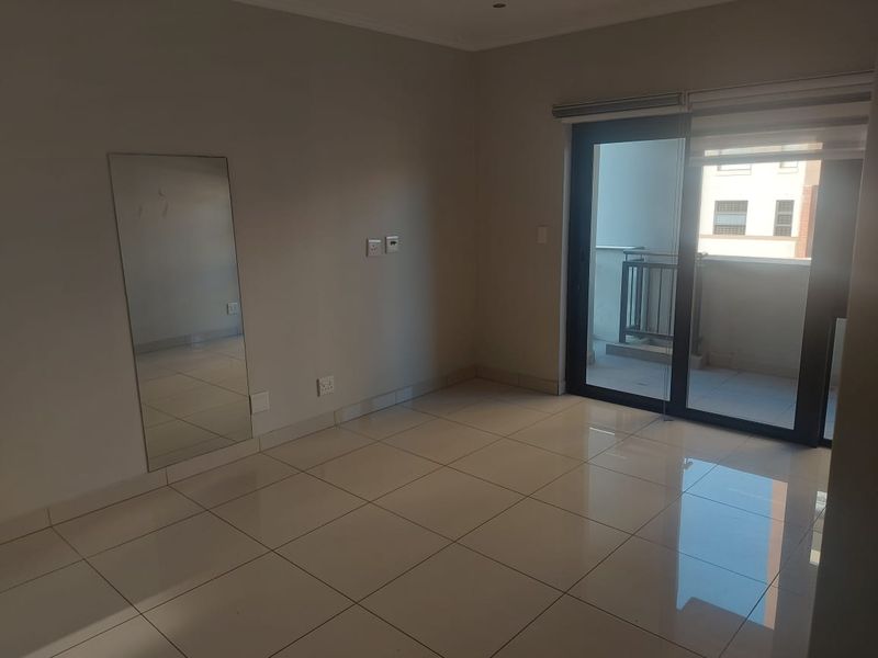 A bright, empty living area featuring neutral tiled flooring, recessed lighting, and a sliding glass door providing access to a private balcony.