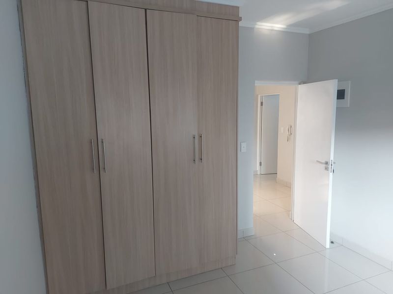 A clean, modern bedroom featuring light wood-finish built-in wardrobes, neutral tiled flooring, and a bright, minimalist aesthetic.