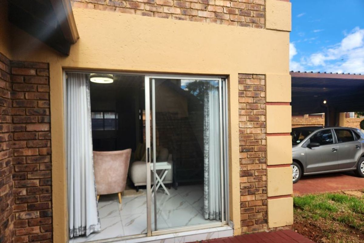 Rear view of the townhouse featuring a sliding glass door entrance, brick exterior walls, and an adjacent paved carport area.