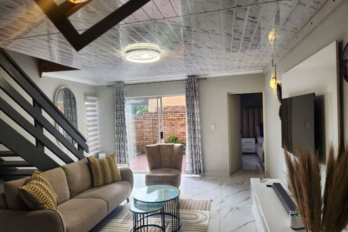 Open-plan living area featuring marble-effect flooring and ceiling panels, with a staircase and sliding door access to the rear patio.