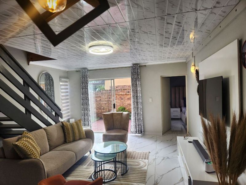 Open-plan living area featuring marble-effect flooring and ceiling panels, with a staircase and sliding door access to the rear patio.