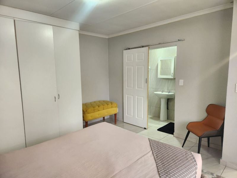 A bedroom featuring built-in cupboards and an en-suite bathroom with a pedestal basin, finished with neutral wall tones and tiled flooring.