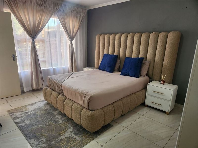 A well-maintained bedroom featuring tiled flooring, a neutral color palette, and an accent wall, providing a comfortable and functional living space.