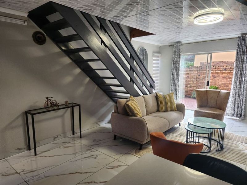 Open-plan living area featuring a modern staircase, marble-look floor tiles, and sliding glass doors providing access to the rear patio.