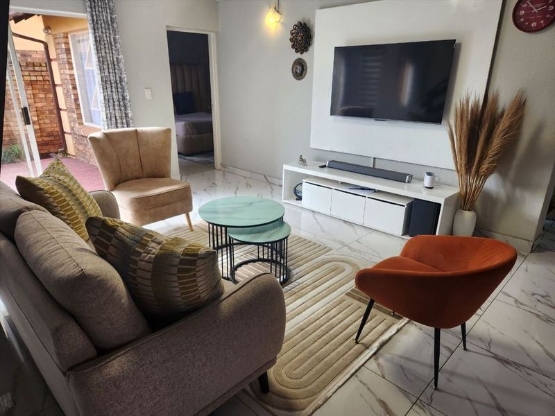 A well-maintained living room featuring modern marble-look floor tiles, a sleek built-in media wall, and direct access to an outdoor patio area.