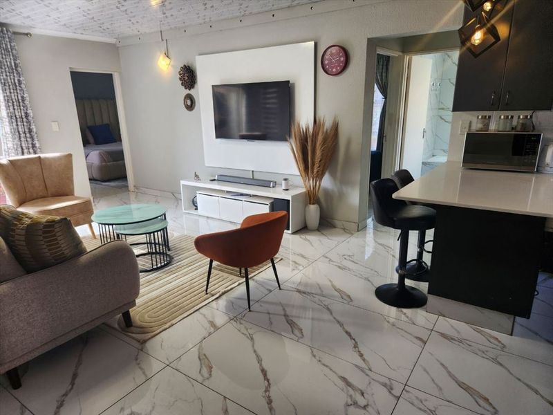 Modern open-plan living area featuring large-format marble-look floor tiles, a sleek built-in media wall, and a functional kitchen breakfast bar.