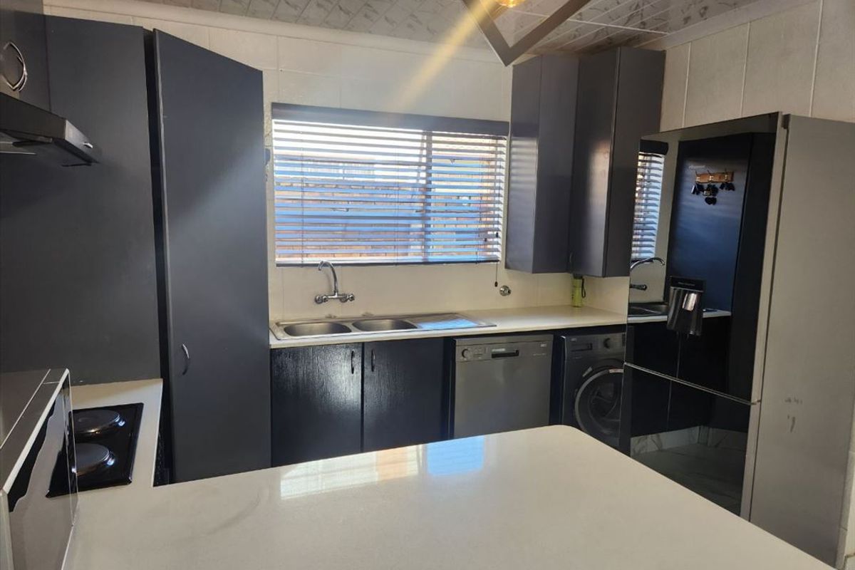 Functional kitchen featuring dark cabinetry, stone countertops, integrated hob, and double sink with a window view.