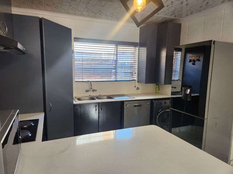 Functional kitchen featuring dark cabinetry, stone countertops, integrated hob, and double sink with a window view.