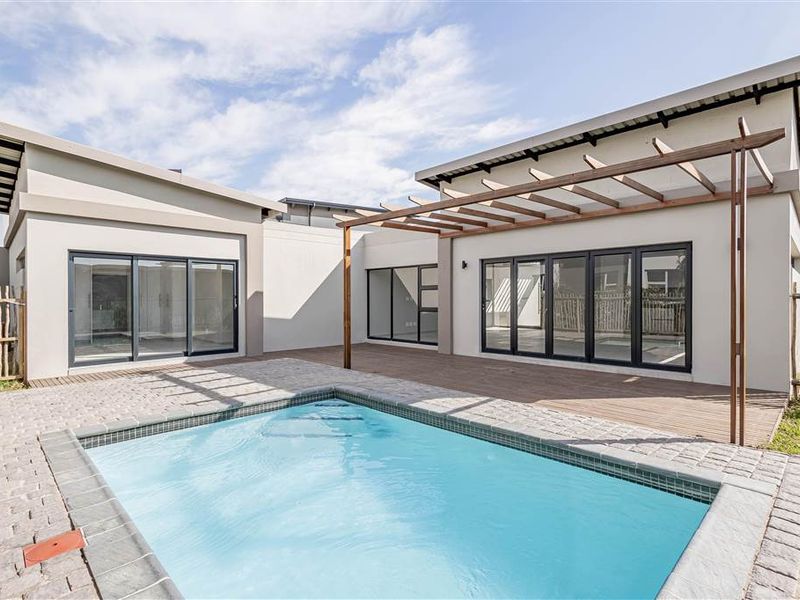 Modern outdoor living area featuring a swimming pool, timber decking, and a pergola, seamlessly connected to the home via large glass sliding and bi-fold doors.