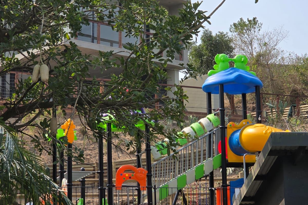 Rear view of a multi-level residential property featuring a terraced garden area with a retaining wall and playground equipment.