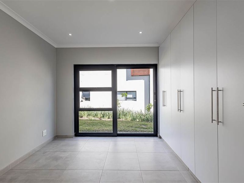 A bright, modern bedroom featuring neutral tiled flooring, extensive built-in storage, and a sliding glass door providing direct access to the garden.