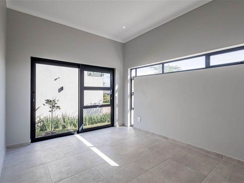 A bright, modern, and empty bedroom featuring large sliding glass doors, clerestory windows, and neutral tiled flooring.