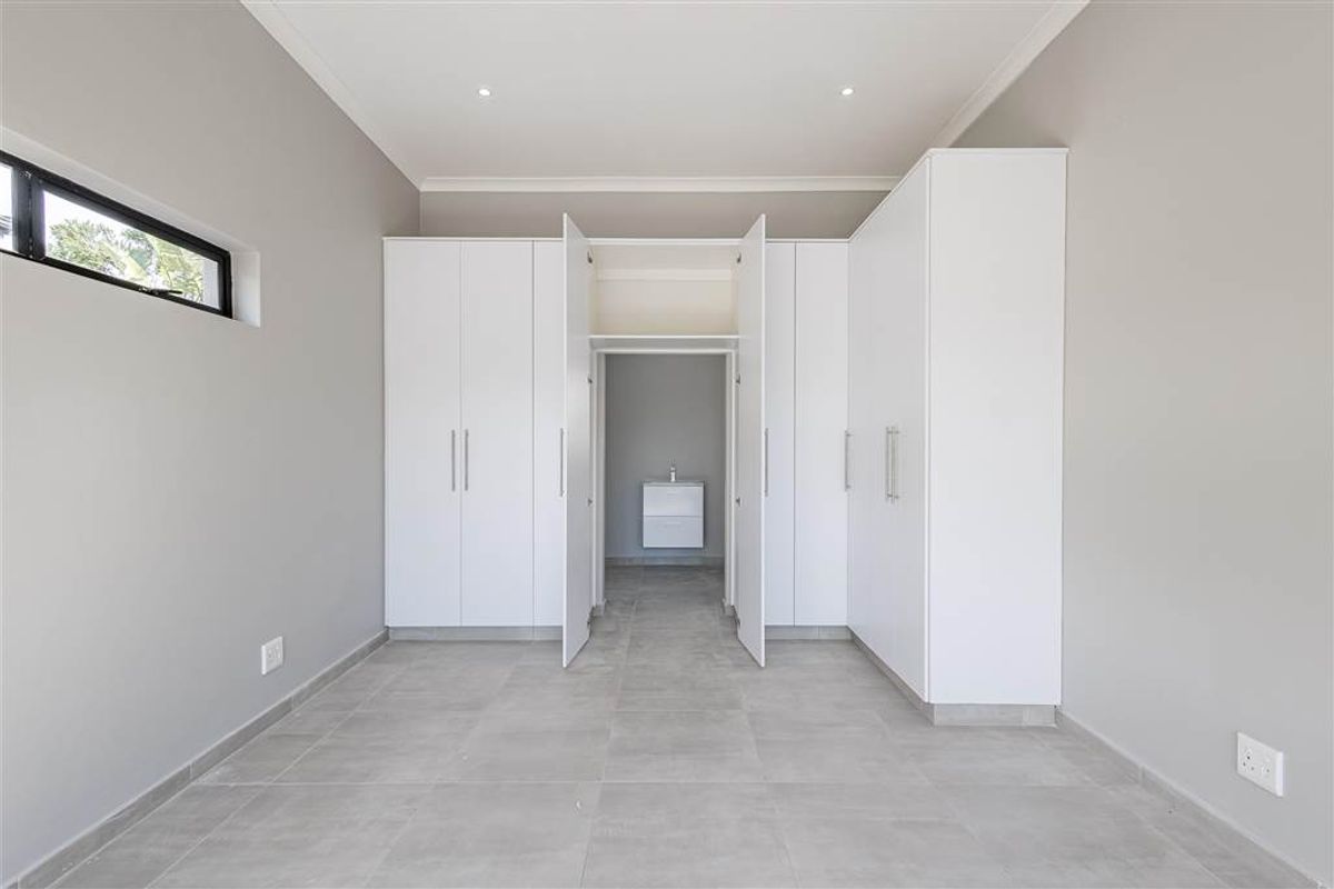 A modern, minimalist bedroom featuring extensive built-in cabinetry, neutral tiled flooring, and a private en-suite vanity area.