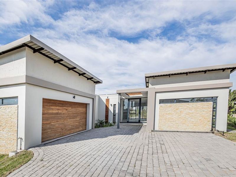 Modern architectural front facade featuring a paved driveway, timber garage door, stone cladding accents, and a prominent glass entrance.