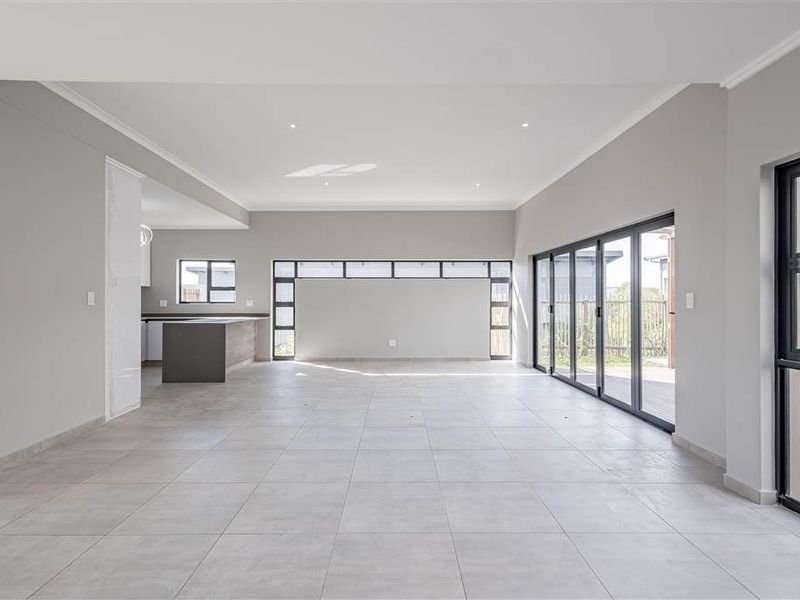 Spacious open-plan living area featuring large aluminium sliding doors, neutral tiled flooring, and a modern kitchen island, offering a bright and versatile layout.