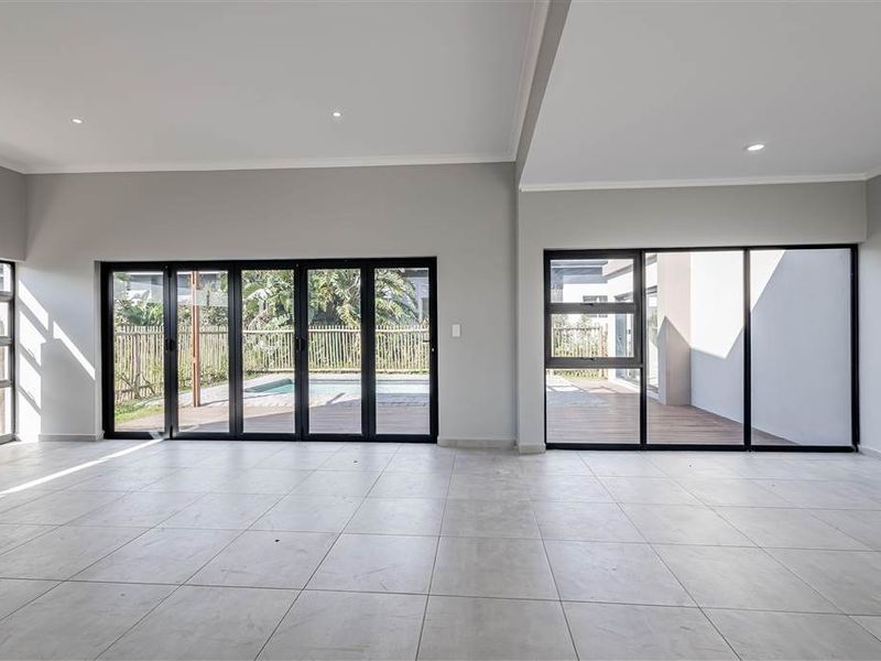 Spacious, modern living area featuring large format floor tiles, recessed lighting, and expansive black aluminium doors opening to the outdoor pool and patio area.