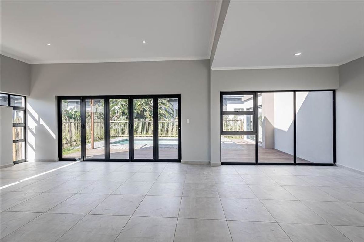 Spacious, modern living area featuring large format floor tiles, recessed lighting, and expansive black aluminium doors opening to the outdoor pool and patio area.