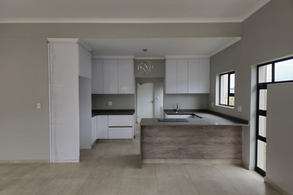 Modern open-plan kitchen featuring sleek white cabinetry, dark stone countertops, integrated hob, and neutral tiled flooring in a clean, contemporary space.