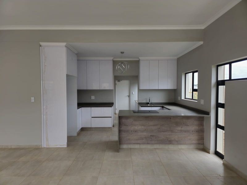 Modern open-plan kitchen featuring sleek white cabinetry, dark stone countertops, integrated hob, and neutral tiled flooring in a clean, contemporary space.