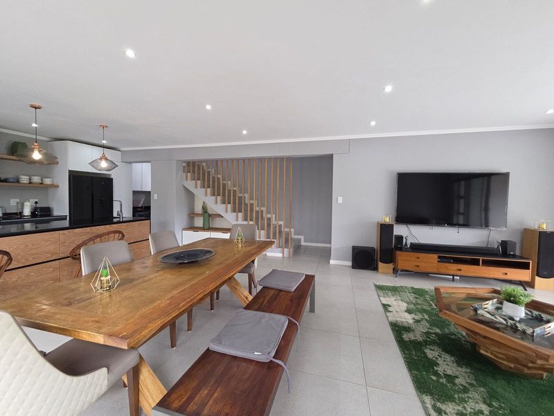 Modern open-plan living, dining, and kitchen area featuring contemporary cabinetry, tiled floors, and a striking timber staircase with a vertical slat balustrade.